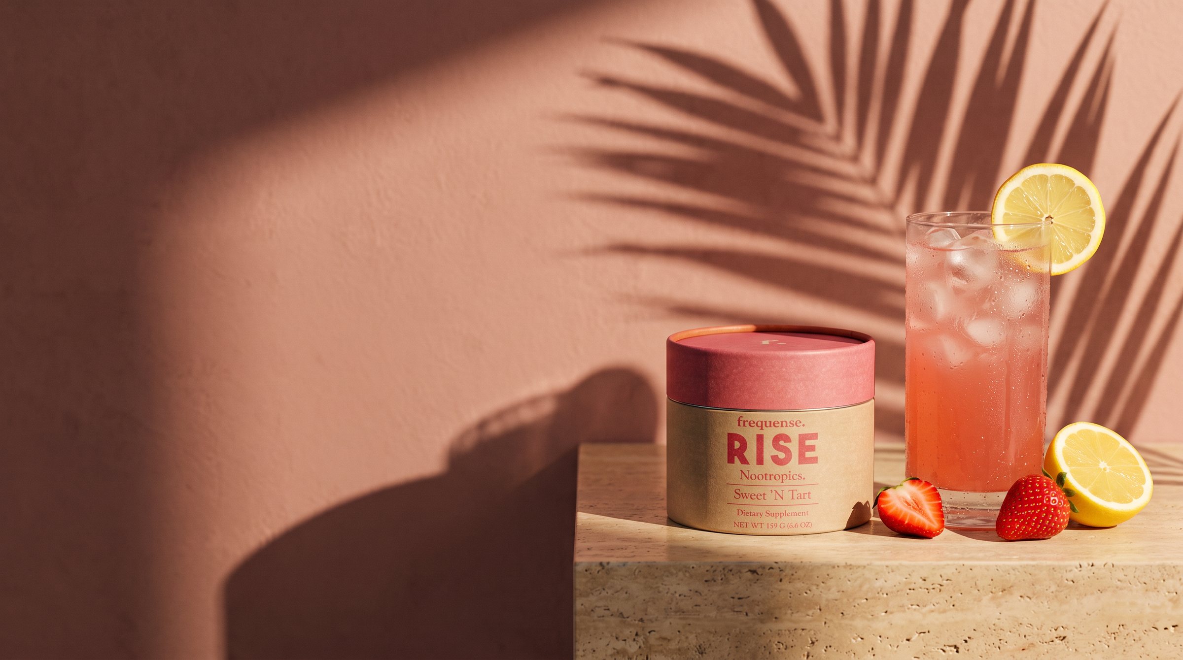 RISE Sweet 'N Tart jar on a travertine ledge beside iced strawberry lemonade, sunset palm shadows on a warm rose wall.