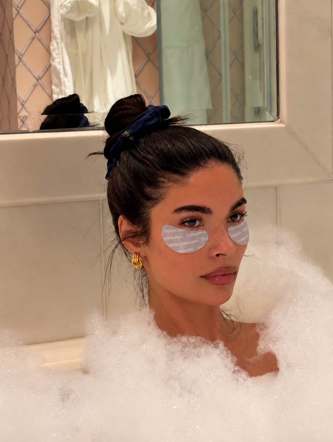 Woman relaxing in a bubble bath wearing Frequense Peptide Eye Masks