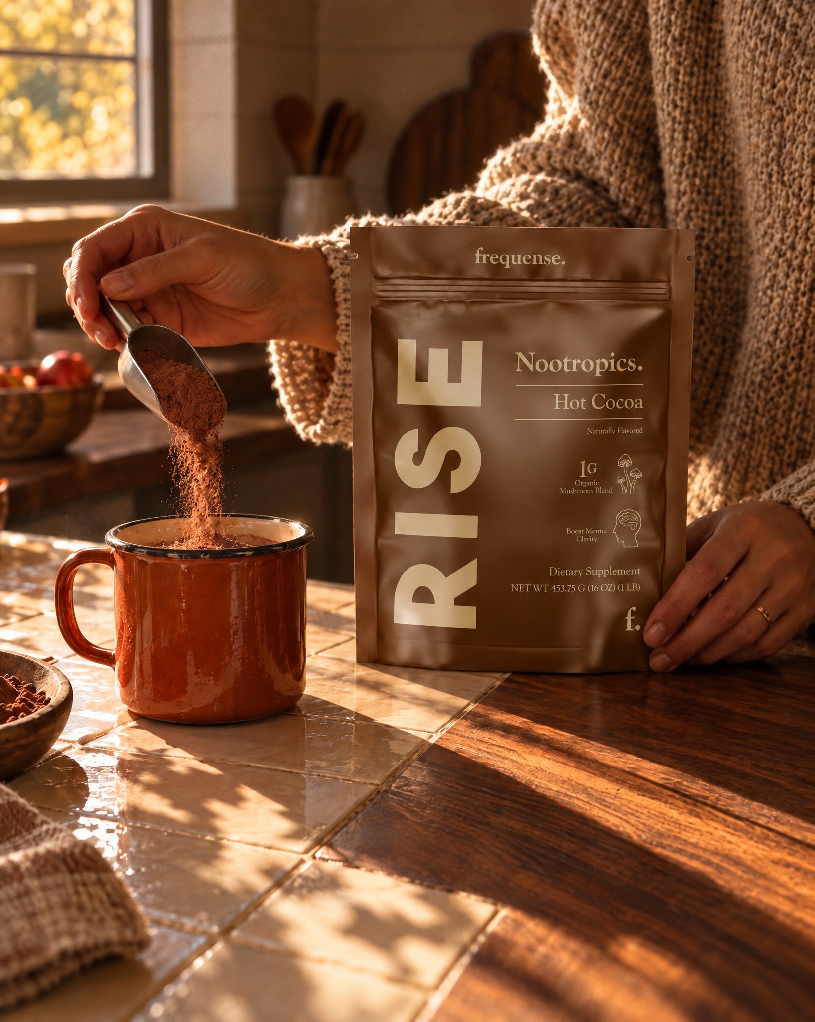 Scooping RISE Hot Cocoa powder into an enamel mug on a sunlit kitchen counter, the pouch held beside it.