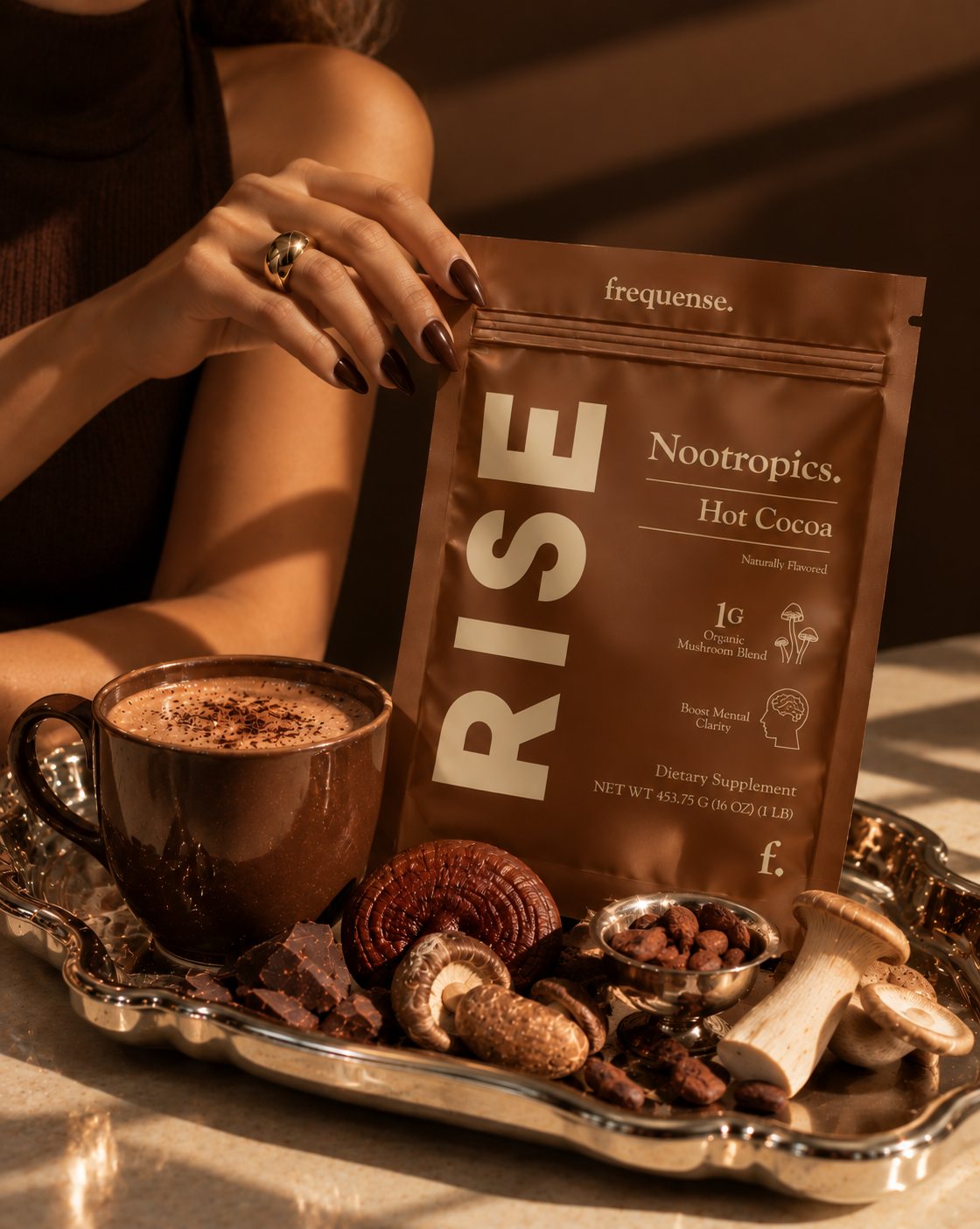 RISE Hot Cocoa pouch on a silver tray with a mug of cocoa, dark chocolate, cacao beans and whole mushrooms.